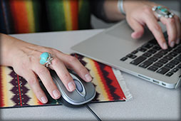 Woman typing on a laptop and holding a computer mouse