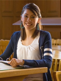 Woman student smiling while sitting in a chair with book in hand.