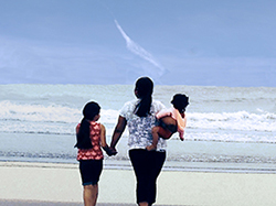 A mother and two children facing the shore at the beach