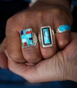 a hand wearing turquiose rings clutching another hand