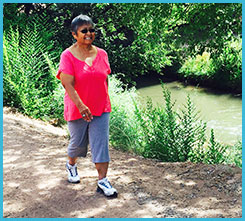 A woman walking on a trail next to a creek.