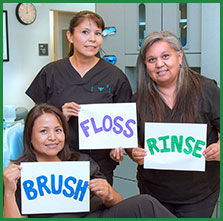 Three women smiling and holding signs that say Brush, Floss and Rinse.