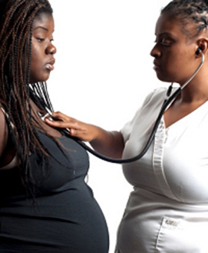 African American midwife and pregnant patient in medical exam.