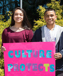 A teenage girl and boy holding a sign that reads culture protects
