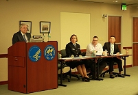 Thumbnail - clicking will open full size image - IHS Principal Deputy Director, Mr. Robert McSwain, addresses the meeting from a podium while other members of IHS leadership seated at the front of the room look on, including Chief Medical Officer, Dr. Susan V. Karol, M.D., Senior Advisor to the Director, Mr. Geoffrey Roth, and Director of the Office of Clinical and Preventive Services, Dr. Alec Thundercloud, M.D.