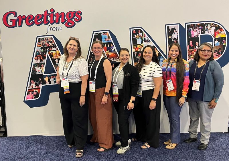 Staff memebers from the Office of the Human Resources and Division of Nursing Services in front of a wall with Greetings from AANP
