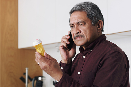 Man on the phone looking at a pill bottle with concern