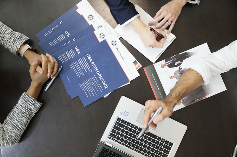 Bird's eye view of a table where people are sitting with USA performance paper work