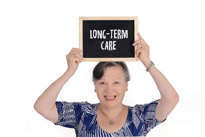 Older woman holding a chalkboard over her head that says Long Term Care