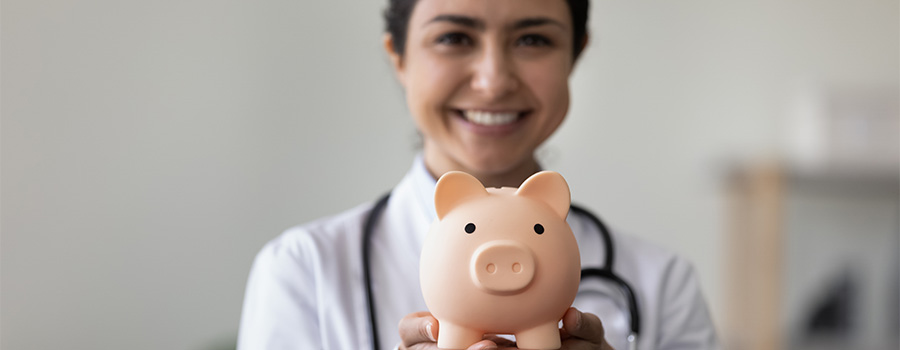 A woman doctor holding a piggybank and smiling widely.