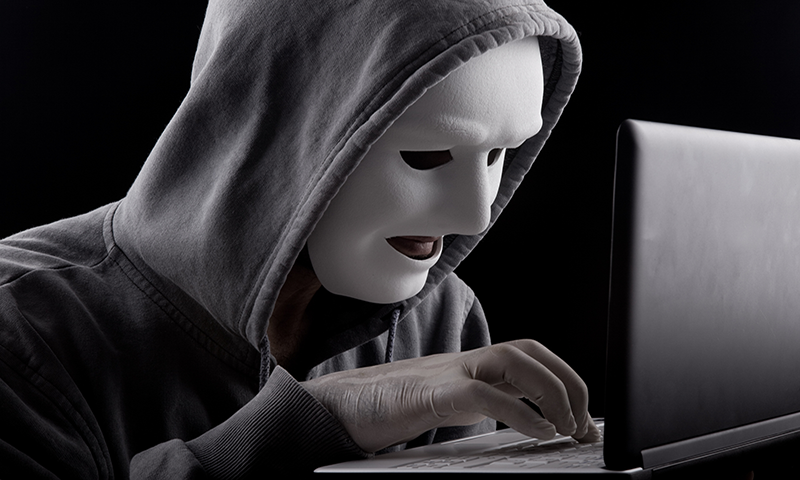 Masked hacker typing on a laptop.