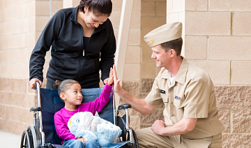 U.S. Public Health Service Officer Kneels Next to Child In Wheelchair