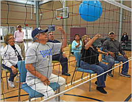 Group of seniors sitting in chairs and playing volleyball.