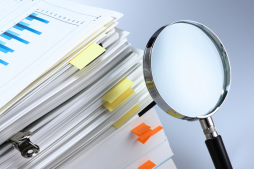 a magnifying glass pointed at a stack of reports